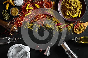 Cooking using fresh ground spices with mortar and small bowls of spice on a black table with powder spillage on its