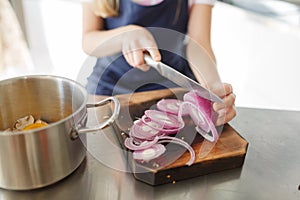 Cooking with vegetables. Female hands cut onions on a wooden board.