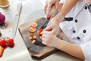 Cooking with vegetables. Little boy`s hands are cutting different ingredients for a salad on a wooden board.