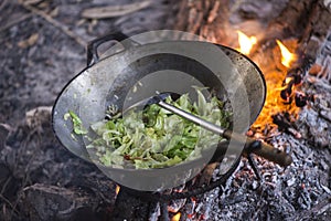 Cooking vegetables and meat in wok pan at camp