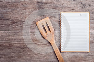 Cooking wooden spatula and lined paper on wooden table top view