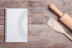 Cooking wooden spatula, rolling pin and lined paper on wooden ta