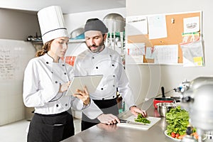 Cooks Using Tablet Computer In Restaurant Kitchen