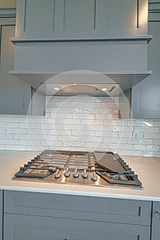 Cooktop and exhaust hood against gray cabinets and white backsplash of kitchen
