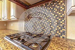 Cooktop under an exhaust hood and faucet mounted on the tile backsplash