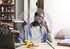 Cool African American guy making phone call while having breakfast in cafe