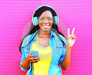 Cool african girl in headphones listens to music over pink