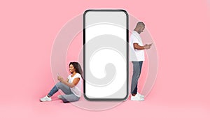 Cool application. Black couple near giant smartphone with blank white screen using gadgets, mock up, full body length