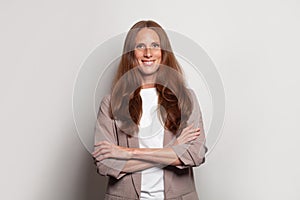 Cool attractive business lady with long brown hairstyle friendly smiling standing with arms crossed against white studio wall