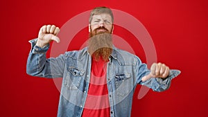 Cool, bearded redhead guy giving thumbs down â€” a negative sign of failure in casual lifestyle fashion, standing over an isolated