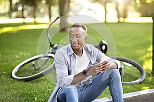 Cool black guy with modern bike using smartphone at park