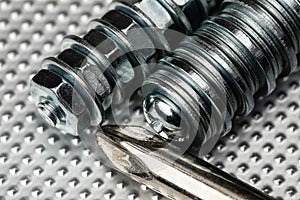 Cool blue toned macro of small bolts with nuts and washers on an industrial steel surface with the top of a phillips head