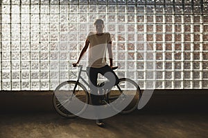 Cool boy standing with classic bicycle and thoughtfully looking in camera. Photo of young man in white t-shirt leaning