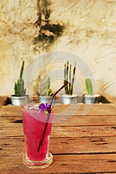 Cool butterfly pea juice on wooden table decorate by cactus in aluminum pots and rough Cement wall