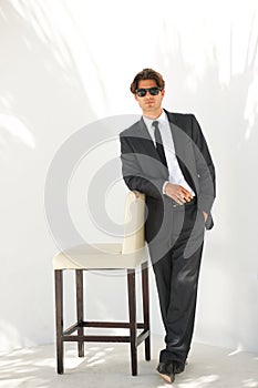 Cool, calm and collected. Full-length portrait of a businessman in a suit and sunglasses leaning on a chair.