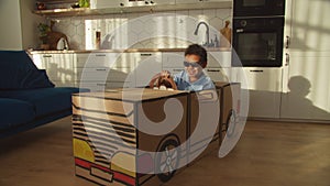 Cool carefree elementary age African boy in sunglasses driving toy cardboard car