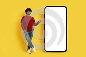 Cool casual indian guy pointing at smartphone with white screen