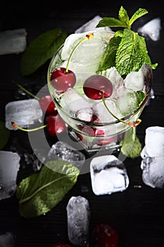 Cool cherry lemonade in a glass with ice and mint. Mint leaves in a glass. Seasonal summer drink. Photo on a black background