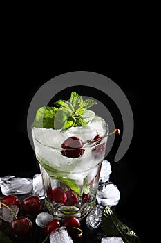 Cool cherry lemonade in a glass with ice and mint. Mint leaves in a glass. Seasonal summer drink. Photo on a black background.