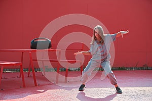Cool child girl dancing with wireless outdoor speaker outside on red background. Dance school advertisement