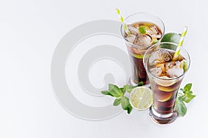 Cool cocktail rum and cola in glasses with bubbles, ice cubes, lime, leaf mint on soft light white background with copy space.