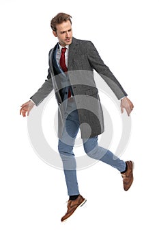 Cool dynamic young man in suit with jacket looking to side and jumping up