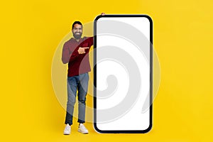 Cool eastern man pointing at huge smartphone with blank screen