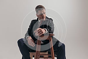 Cool elegant man looking to side and holding elbow on wooden chair