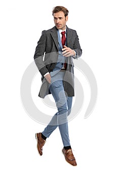 Cool elegant young man in suit with grey coat looking to side and jumping