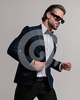 cool fashion businessman with sunglasses looking to side and unbuttoning suit