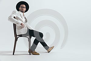 cool fashion man with hat holding arm on chair and sitting