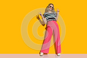 Cool fashion model in pink loose pants and sunglasses is showing peace hand sign