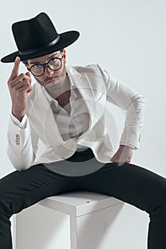 cool fashion sexy man with glasses adjusting hat while sitting