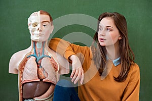 Cool female high school student portrait with an artificial human body model. Student having fun in Biology class.