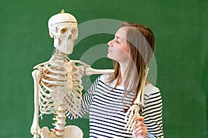 Cool female high school student portrait with an artificial human body skeleton. Student having fun in Biology class.