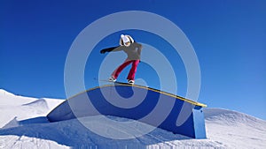 Cool female snowboarder does a jib trick along a railing in a big snow park.