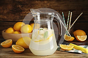 Cool freshly made lemonade in glass pitcher and fresh fruits on wooden table