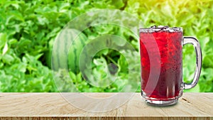 Cool freshly Watermelon juice in a glass on wooden table with watermelon farm background, Summer drinks with ice