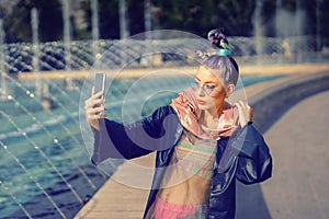 Cool funky hipster young fashion influencer girl with crazy hair and avant garde style taking selfie on street photo