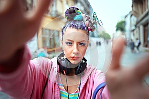 Cool funky young girl with headphones and crazy hair enjoy power of music taking selfie on street