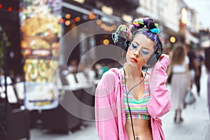 Cool funky young hipster woman with trendy eyeglasses and crazy hair listening music on headphones outdoor