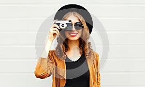 Cool funny girl model with retro film camera wearing a elegant hat, brown jacket