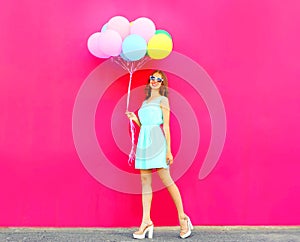 Cool girl with an air colorful balloons walking over a pink