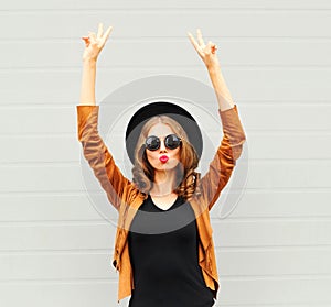 Cool girl in black round hat, sunglasses and jacket raises hands