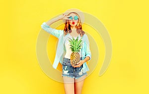 cool girl with pineapple blowing red lips sending sweet air kiss in summer straw hat, sunglasses, shorts on colorful yellow