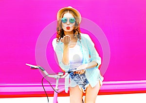 Cool girl sends air kiss on bicycle over colorful pink