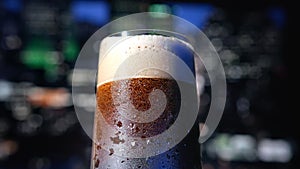 Cool glass of dark craft beer or soda in bar of nightclub, closeup view against night city panorama