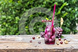 Cool grape juice in glass jar on old wood with tree background.