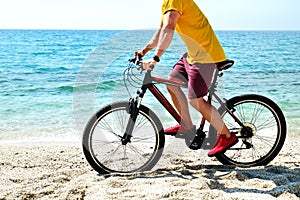 Cool guy on the beach riding mountain bike with black and red frame o over ocean background