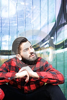 Cool guy with beard and piercings sitting outdoors